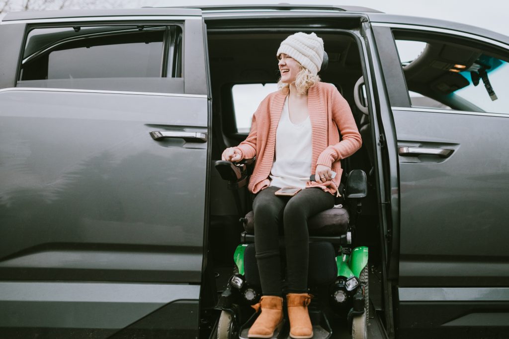 An independent young adult woman with cerebral palsy going about some of her daily routines. She rides her wheelchair up a ramp in her accessible van, preparing to drive to her job.