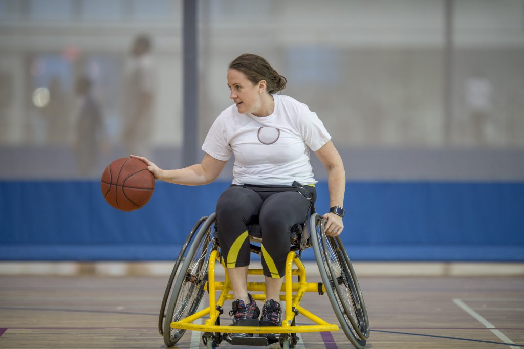 A physically impaired woman is bouncing a basketball while in a wheelchair.