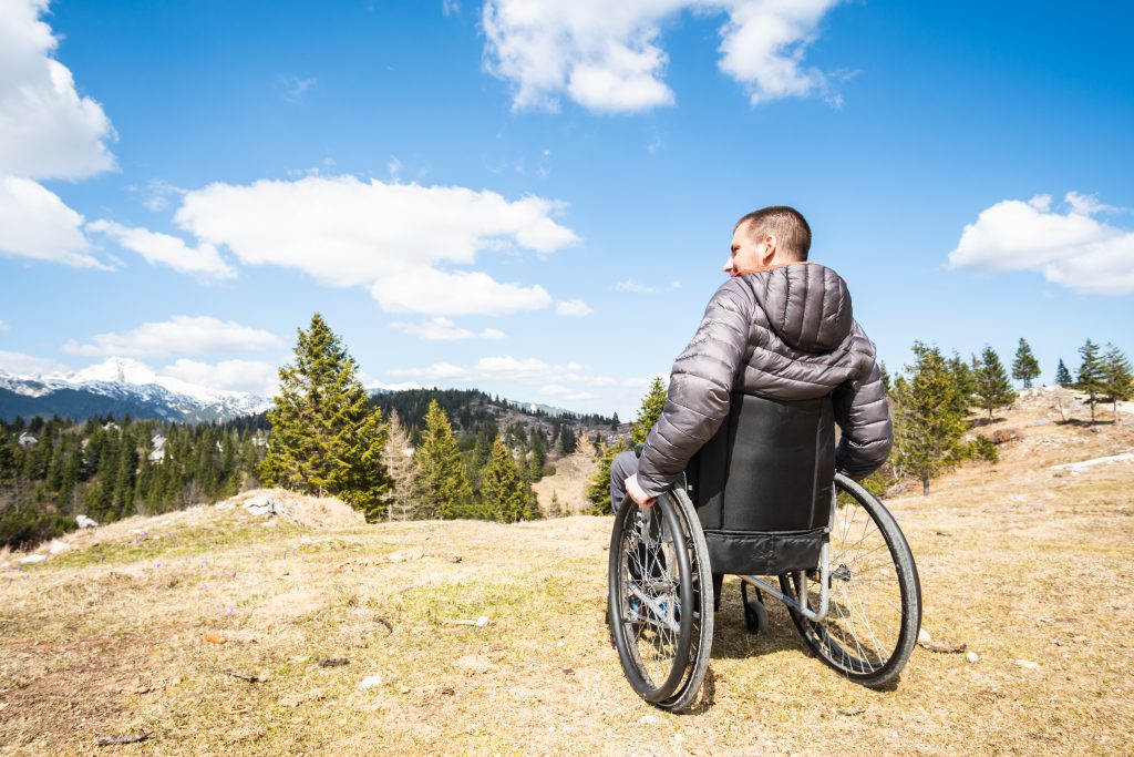 Young disabled man in wheelchair outside in nature observing mountains and nature